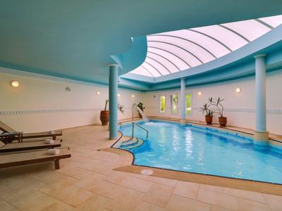 Krytý bazén s lehátky a velkým zakřiveným světlíkem.