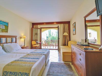 Helles Hotelzimmer mit Doppelbett, Balkon und Holzmöbeln bei Tageslicht.