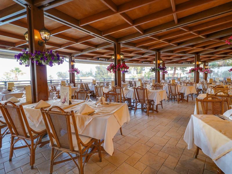 Prostorná restaurace s prostřenými stoly, dřevěným stropem a světlou dlažbou.