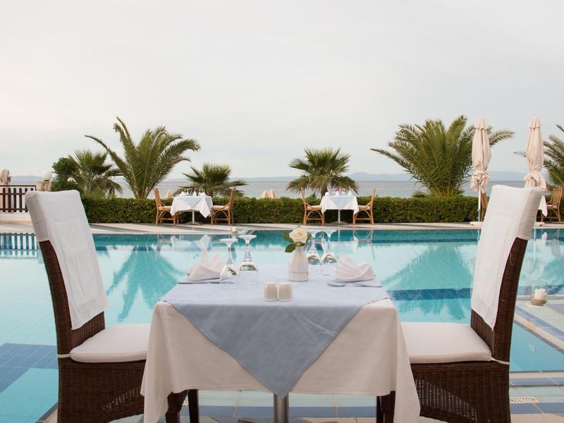 Elegantně prostřený stůl u bazénu s palmami a výhledem na moře.