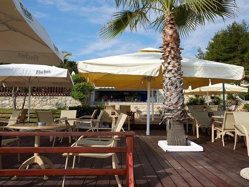 Terasa restaurace s bílými slunečníky a palmami pod modrou oblohou.