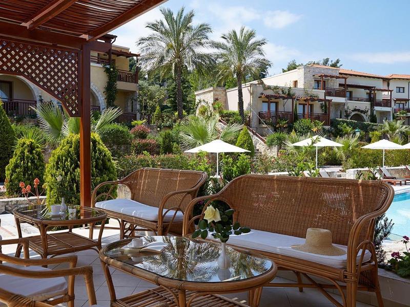 Pohodlná terasa s ratanovým nábytkem, bazénem a palmami pod modrou oblohou.