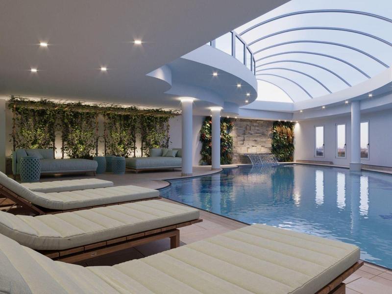 Luxusní vnitřní bazén s denním světlem, lehátky a elegantními zelenými stěnami.