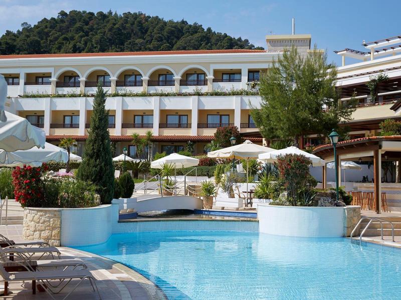 Hotel s venkovním bazénem, slunečníky a lehátky na slunci.