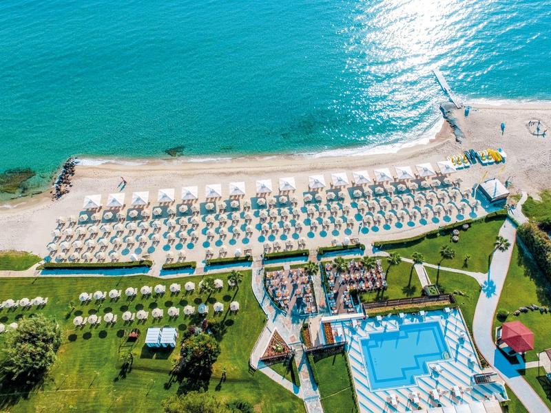 Letecký pohled na pláž s lehátky, bazénem a přilehlým hotelovým areálem u moře.