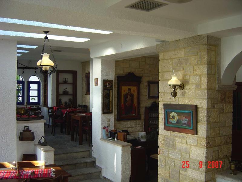 Przytulny hotelowy salon z kamienną ścianą, obrazami i częścią jadalną w tle.