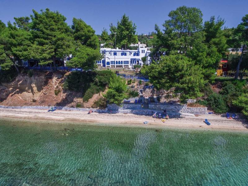 Willa nadmorska otoczona drzewami z widokiem na czystą turkusową wodę i piaszczystą plażę.