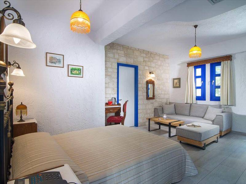 Przytulny pokój z łóżkiem, sofą, niebieskimi ramami okien i ciepłym oświetleniem.