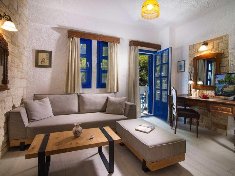 Przytulny salon z beżową sofą, drewnianym stolikiem i otwartymi drzwiami z niebieskimi okiennicami.