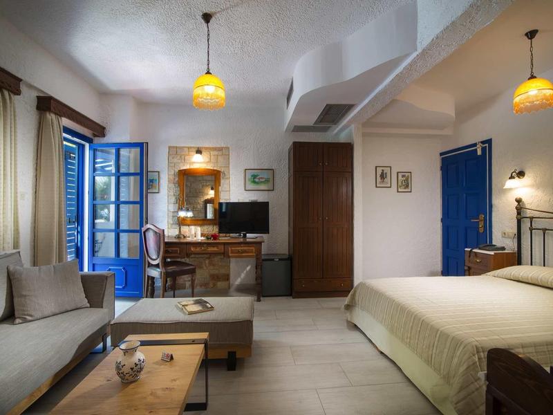 Przytulny pokój hotelowy z łóżkiem, sofą, drewnianymi meblami, niebieskimi drzwiami i ciepłym oświetleniem.