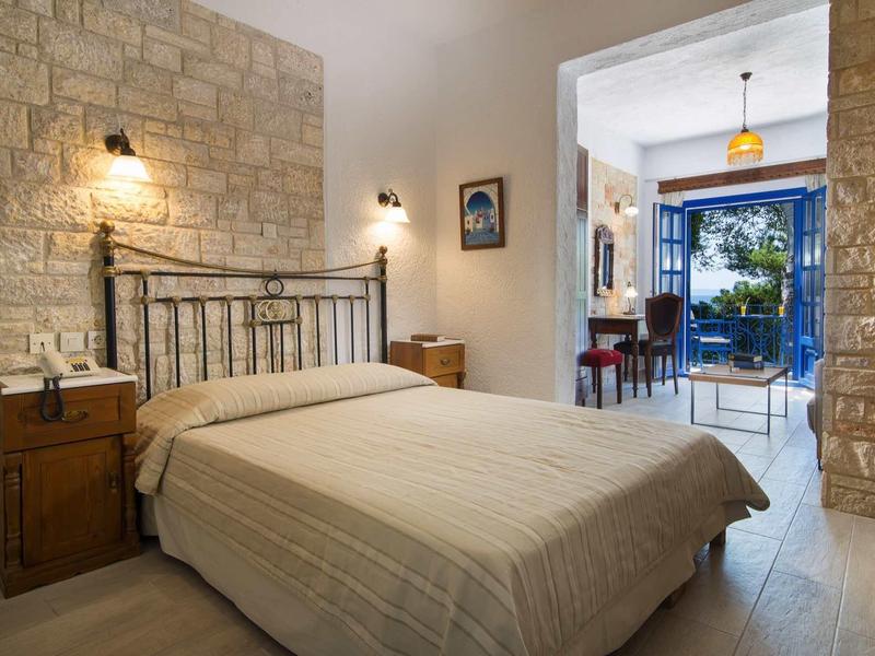 Przytulna sypialnia z kamiennymi ścianami, podwójnym łóżkiem, drewnianymi meblami i widokiem na balkon z zielenią.