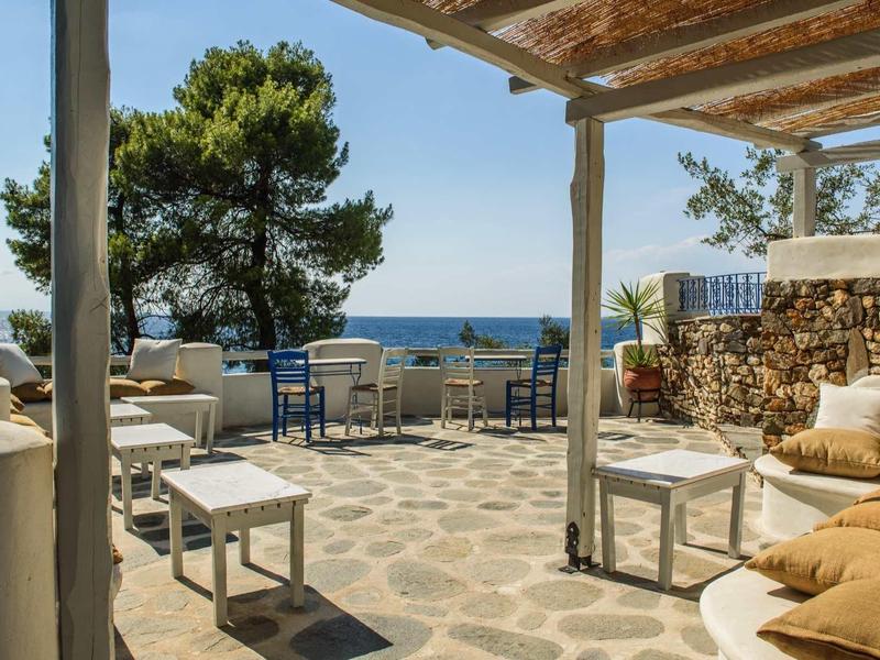 Zewnętrzna przestrzeń wypoczynkowa z sofami i stołami z widokiem na morze pod drewnianą pergolą.