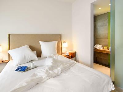 Světle zařízený hotelový pokoj s manželskou postelí a přilehlou koupelnou