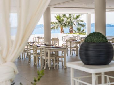 Área abierta del hotel con vista al mar, mesas y sillas blancas y palmeras al fondo.