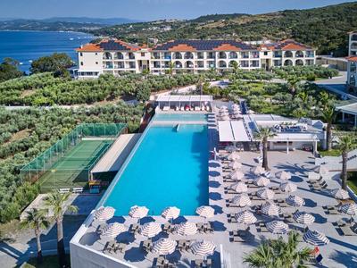 Gran piscina de hotel con sombrillas y tumbonas cerca del mar rodeada de paisaje verde.