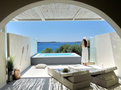 Área exterior moderna con sofá y piscina, vista al mar bajo un cielo azul.