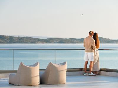 Pareja en terraza con vista al mar, dos cojines en el suelo, ambiente relajado.