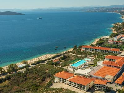 Complejo hotelero con techos rojos cerca de una larga playa de arena y mar azul claro.
