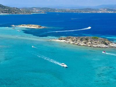 Mar azul claro con pequeñas embarcaciones e islotes rocosos al fondo.