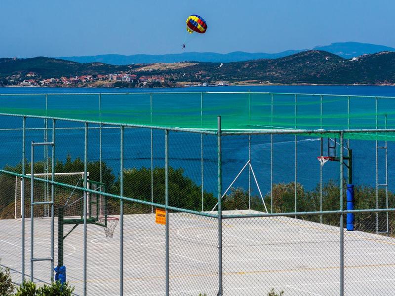 Volejbalová síť před pobřežní krajinou s modrým mořem a horami v pozadí.