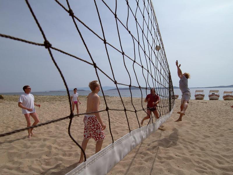 Skupina lidí hrající plážový volejbal na písečné pláži s výhledem na moře.