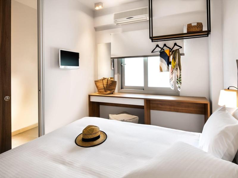 Světlo ložnice s bílým povlečením, stolem pod oknem a televizí na zdi.