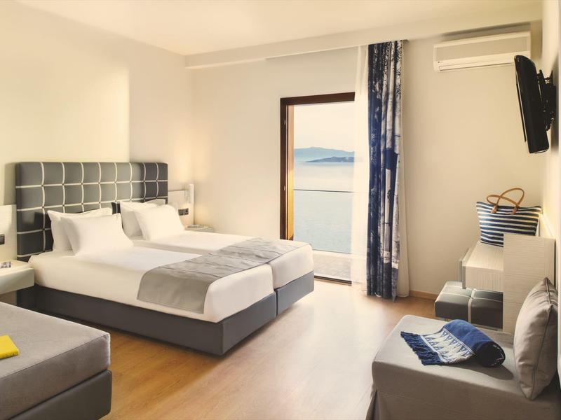 Moderní hotelový pokoj s manželskou postelí, posezením a výhledem na moře přes balkónové dveře