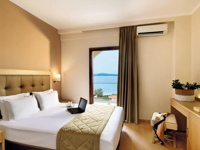 Pohodlný hotelový pokoj s manželskou postelí, notebookem a balkonem s výhledem na moře.