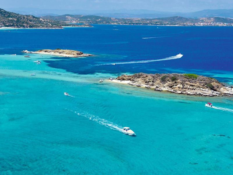 Čisté tyrkysové moře s malými ostrovy a loděmi pod modrou oblohou.