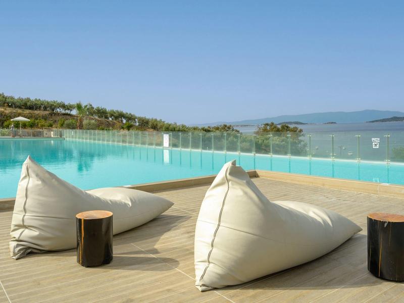 Dva bílé sedací vaky a malé odkládací stolky na dřevěné terase s výhledem na bazén a moře.