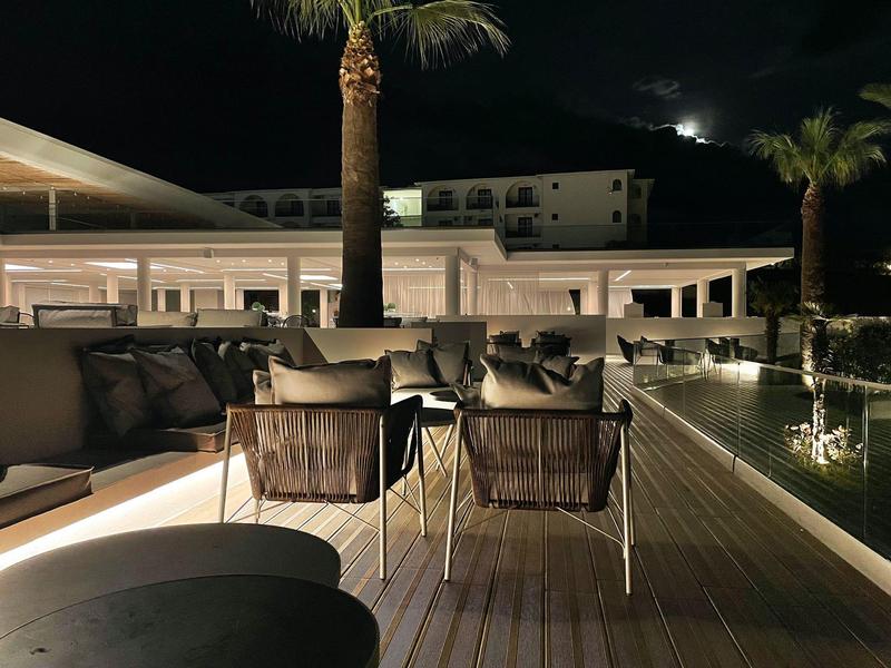 Hotelová terasa v noci s posezením, osvětlená a obklopená palmami.