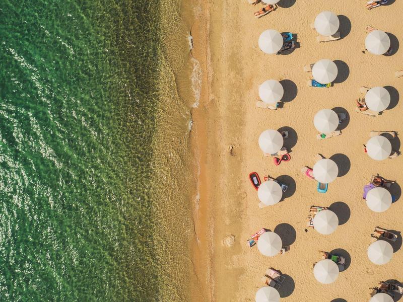 Letecký pohled na pláž s řadami slunečníků a zelenou vodou u břehu.