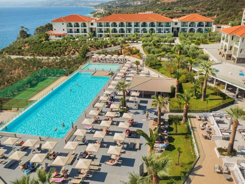 Moderní hotelový bazén s lehátky a výhledem na oceán v kopcovité krajině.