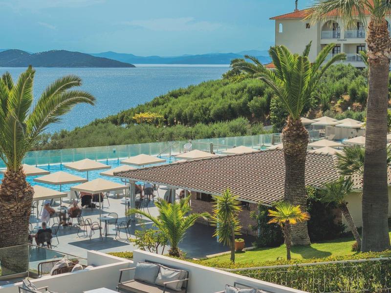 Výhled na terasu s posezením, palmami a lehátky u moře.