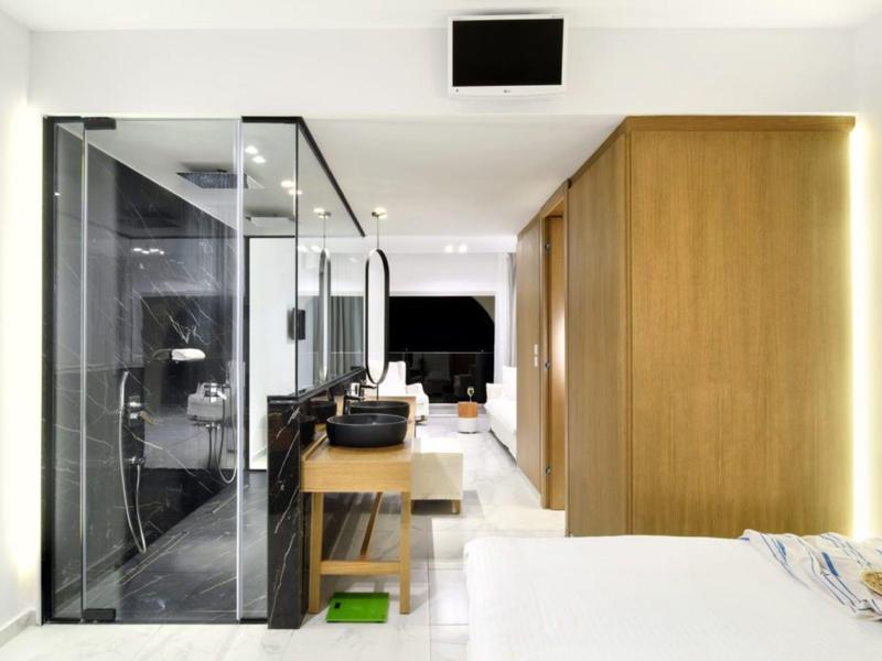 Moderní hotelový pokoj se skleněnou sprchou, dřevěným nábytkem a světlým interiérem