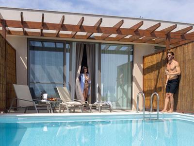 Dva lidé si užívají bazén před moderním hotelovým pokojem s dřevěnou pergolou.