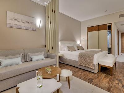 Moderní hotelový pokoj s postelí, pohovkou, malými stolky a dřevěnou podlahou.