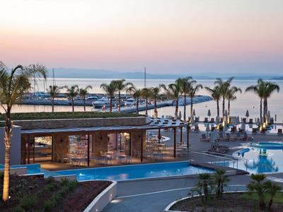 Área moderna de piscina con palmeras y vista al mar al atardecer.