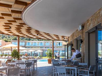 Venkovní jídelní prostor u bazénu s stoly, židlemi, slunečníky a číšníkem.