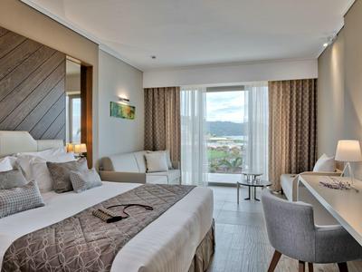 Moderní hotelový pokoj s manželskou postelí, křeslem, psacím stolem a velkým oknem s výhledem.