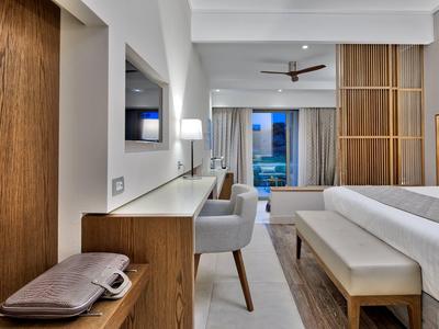 Moderní hotelový pokoj s postelí, lavicí, psacím stolem, židlí a posuvnými dřevěnými dveřmi.