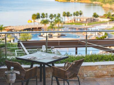 Mesa con dos sillas en terraza con vista al mar y piscina al fondo.