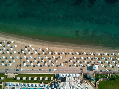 Letecký pohled na pláž s bílými slunečníky a tyrkysovým mořem v resortu.