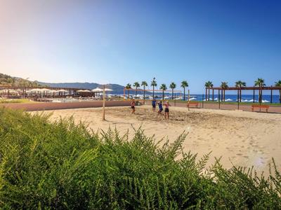Playa con palmeras, arena y personas bajo cielo soleado y mar azul.
