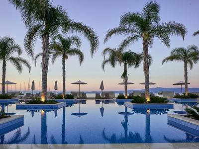 Área de piscina con palmeras y sombrillas junto al mar al atardecer