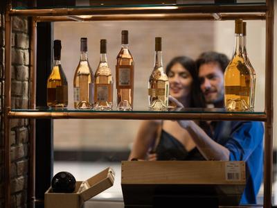 Vista a través de una ventana de una pareja en una cafetería con una fila de botellas de vino en la estantería.