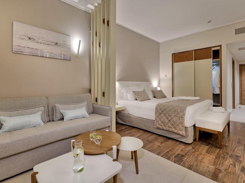 Moderní hotelový pokoj s postelí, pohovkou, malými stolky a dřevěnou podlahou.