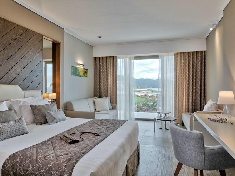 Moderní hotelový pokoj s manželskou postelí, křeslem, psacím stolem a velkým oknem s výhledem.