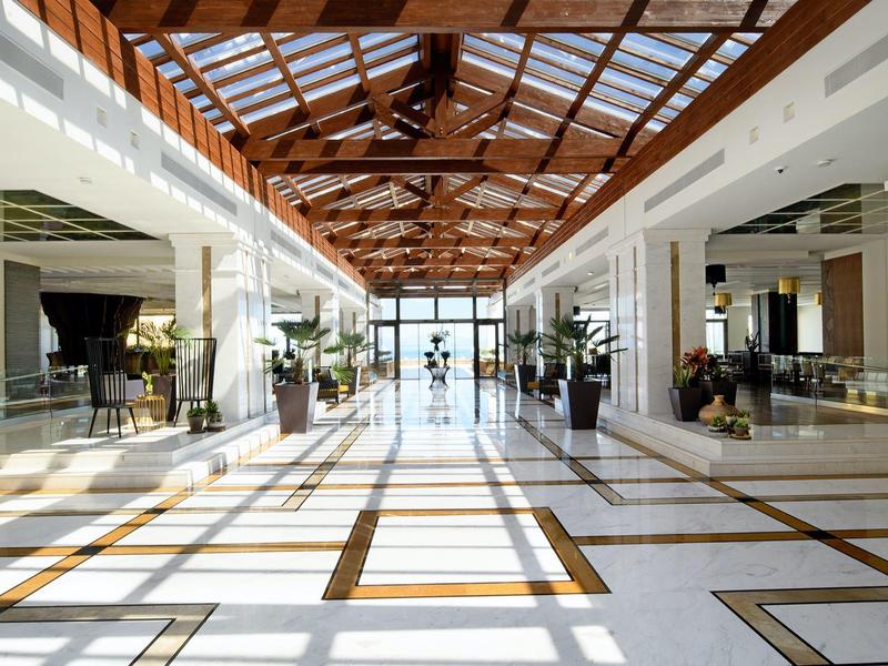 Světlé hotelové lobby s mramorovými podlahami a stropem s dřevěnými trámy.