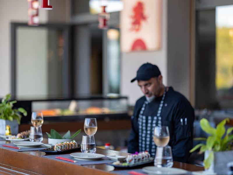 Barman připravující nápoje ve stylovém hotelovém baru s rostlinami a vinnými sklenicemi.